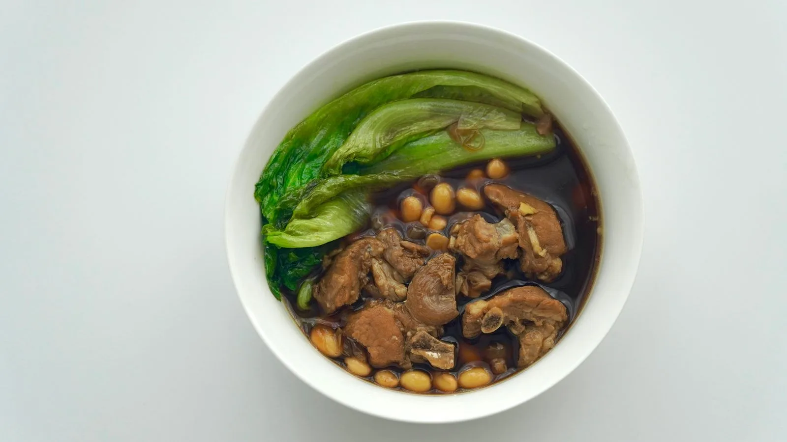 A savory bowl of pork soup with greens and beans, perfect for hearty meals.