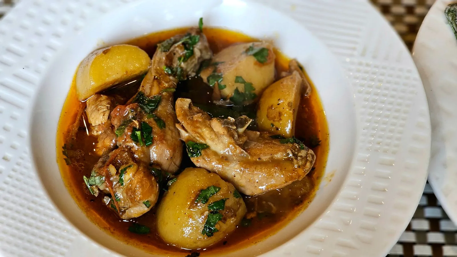 Delicious chicken stew with potatoes, garnished with fresh herbs, served in a white dish.