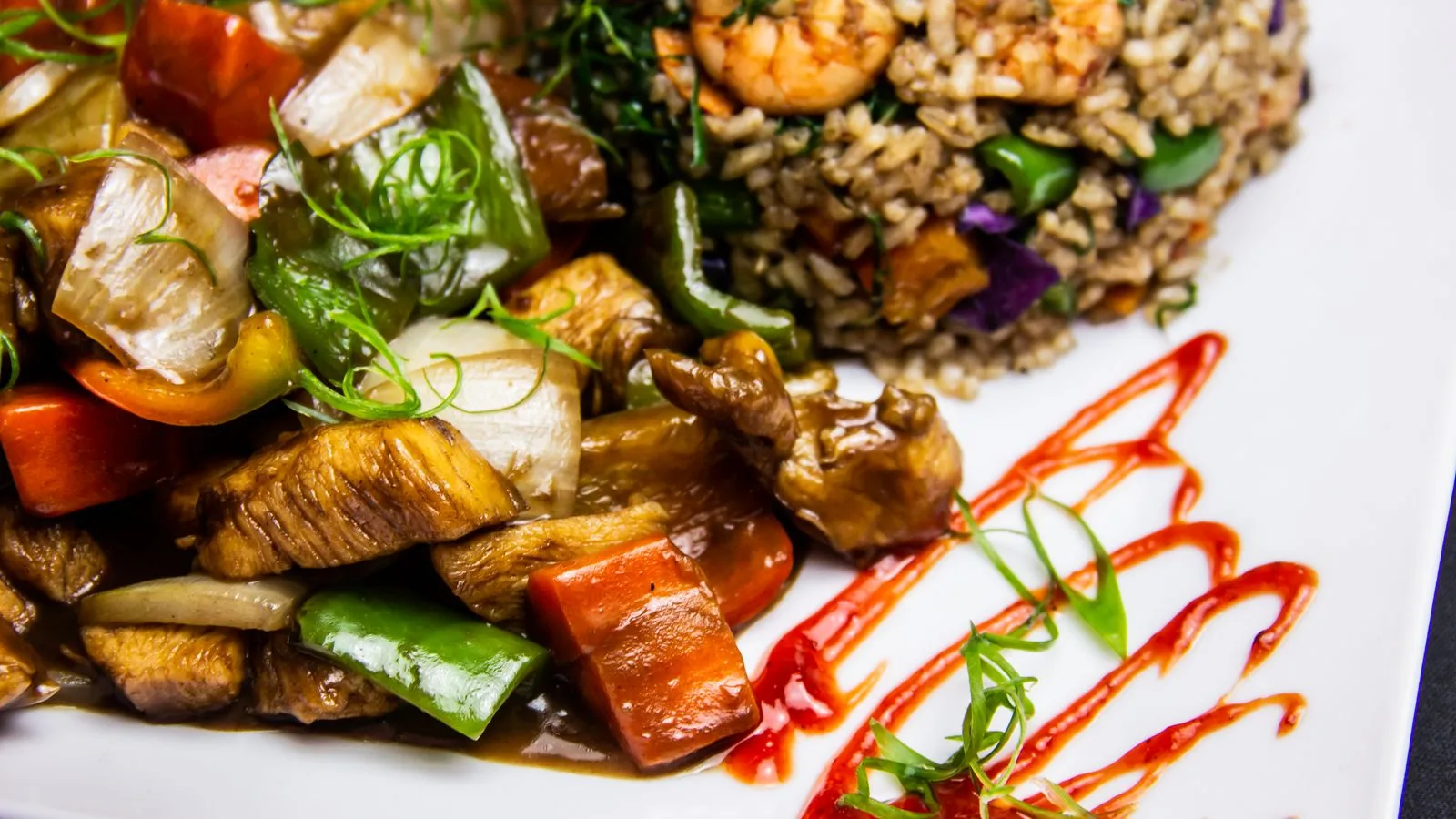 Colorful Brazilian stir fry with shrimp, chicken, and vegetables served on a white plate with sauce garnish.