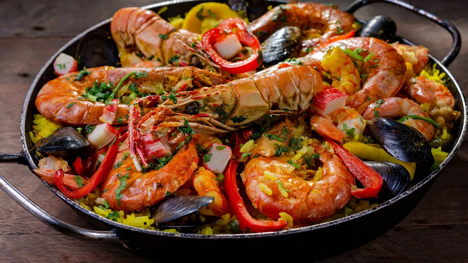 A colorful close-up of a seafood paella with prawns, mussels, and vegetables in a pan.