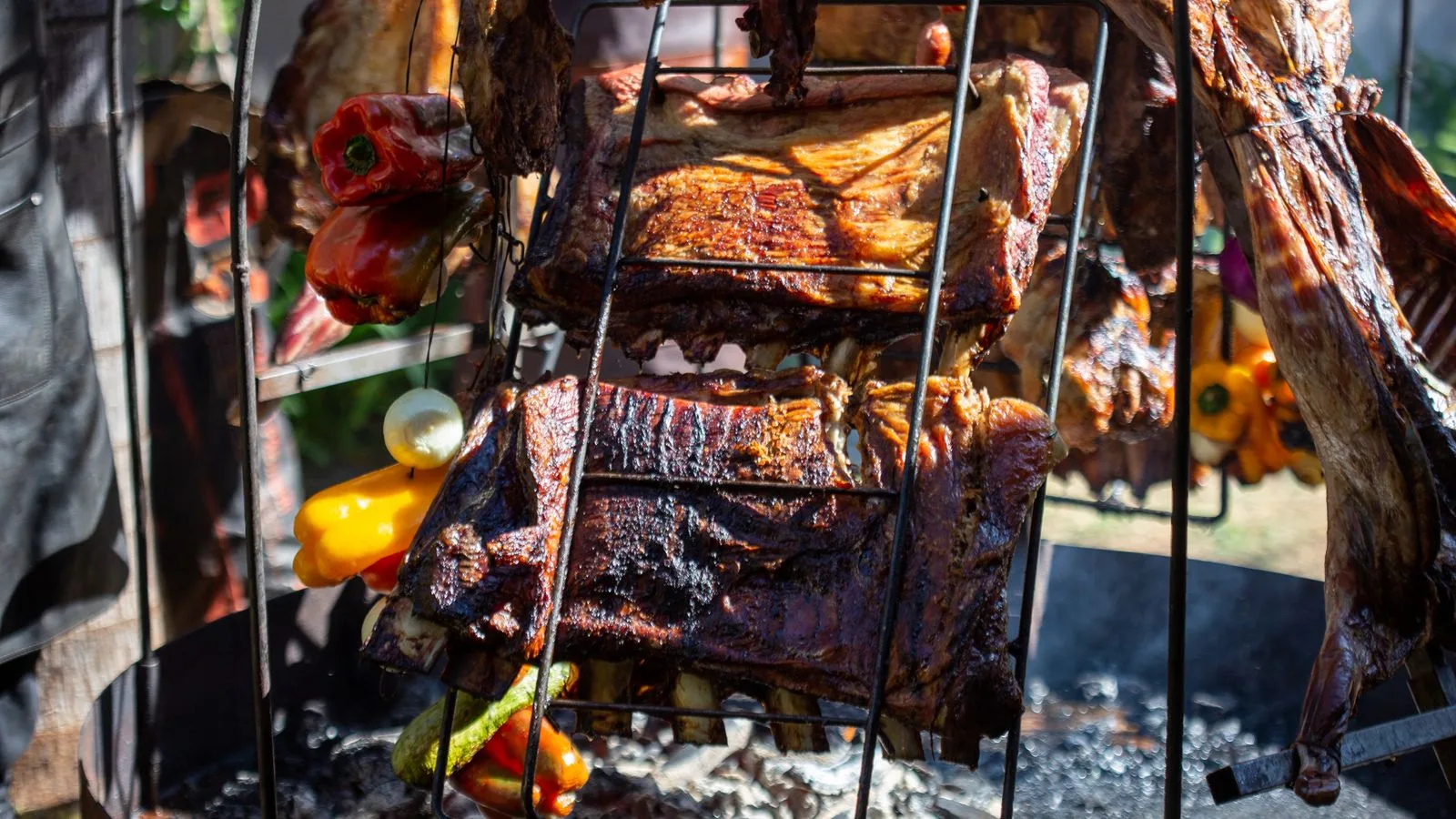 Close-up of roasted ribs and vegetables on an outdoor barbecue grill.