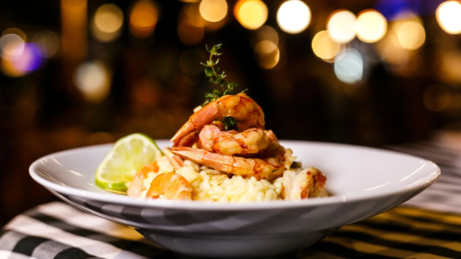 Close-up of a delicious shrimp risotto with bokeh background, garnished with a lime slice.