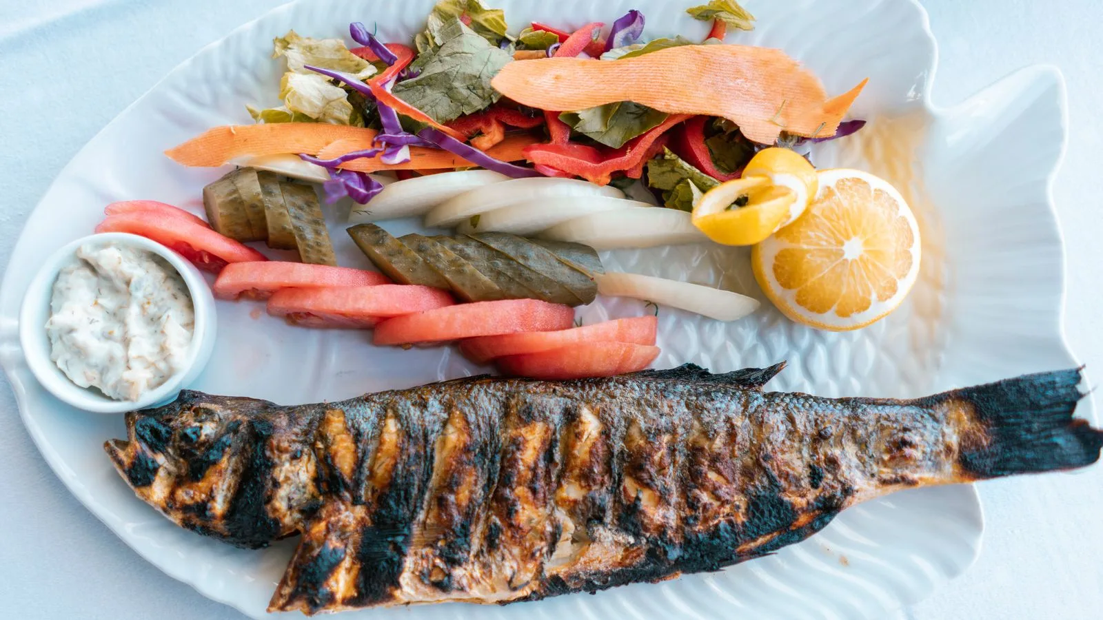 Delicious grilled fish served with fresh vegetables and lemon on a white plate.