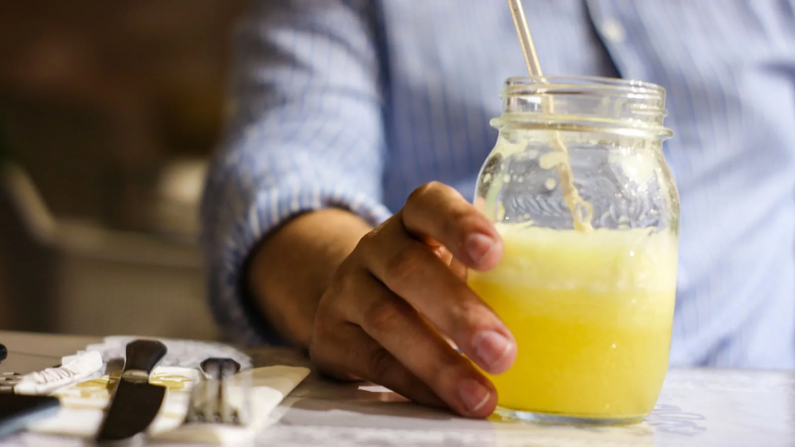 Person holding a refreshing glass jar of lemonade with a straw in an indoor setting.