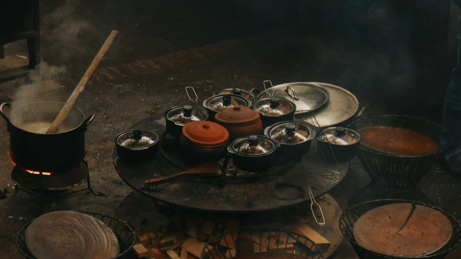 A rustic cooking setup with steaming pots and pans over an open flame.