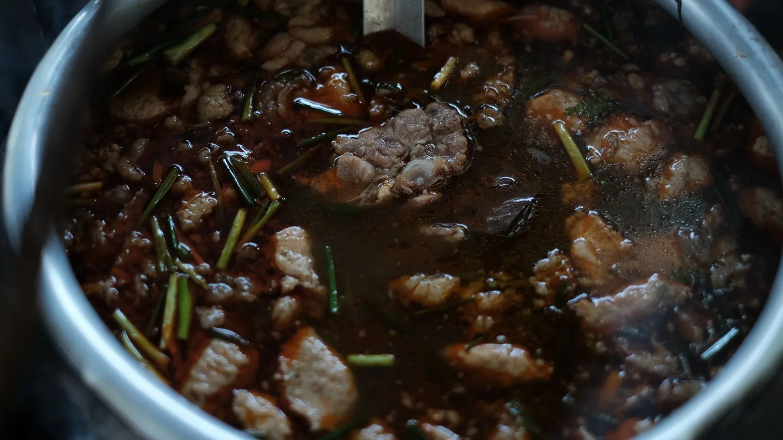 Close-up of a simmering beef stew with herbs and spices in a metal pot.