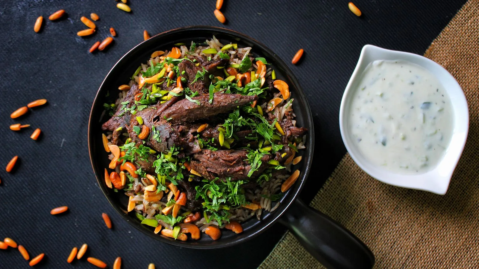 A mouth-watering lamb and rice dish garnished with herbs and nuts, paired with a creamy yogurt sauce.